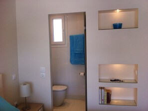 A bathroom with a toilet, a towel hanging on the wall, and shelves with books and a blue bowl.