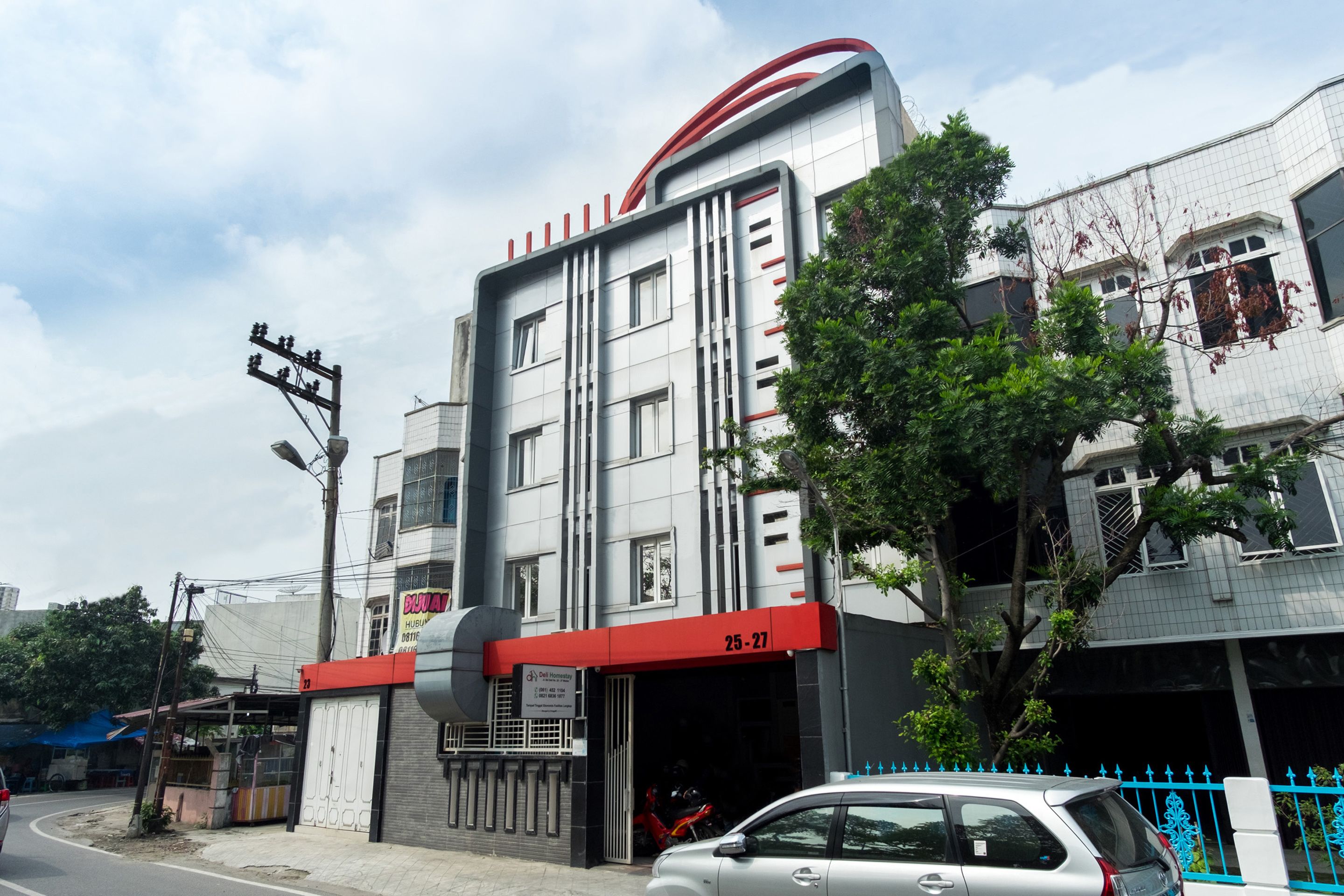 A modern building with a red and white facade, numbered 25-27, and a gated entrance.