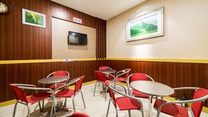 Un área de comedor con sillas y mesas rojas, un reloj y un televisor en la pared.