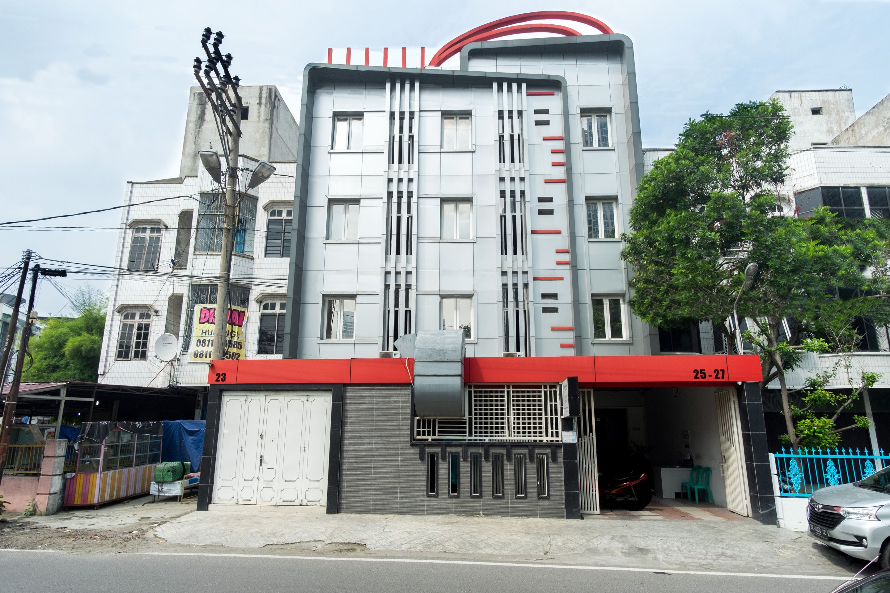 A multi-story building with a red awning, a garage door, and a sign with the number 25-27.