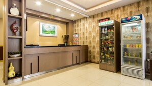 Zona de recepción con mostrador de madera, cartel de bar de aperitivos y máquina expendedora de bebidas.