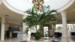 Un hall espacioso con una zona de estar circular central, una palmera grande y un candelabro.