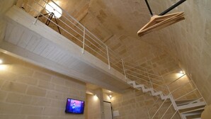 A multi-level interior with a staircase, a television mounted on the wall, and a hanging light fixture. - Comera (Matera)
