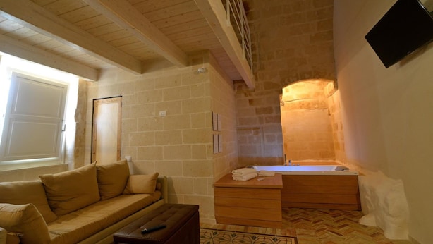 A room with a wooden ceiling, a stone wall, a wooden bench, a sofa, a wooden cabinet, and a bathtub. - Comera (Matera)
