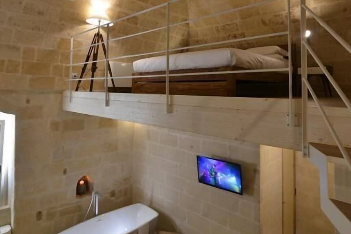 A rustic stone-walled room with a bunk bed, a modern bathtub, and a mounted television.