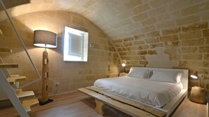 A bedroom with a wooden bed, a wooden bench, a staircase, and a lamp. - Comera (Matera)