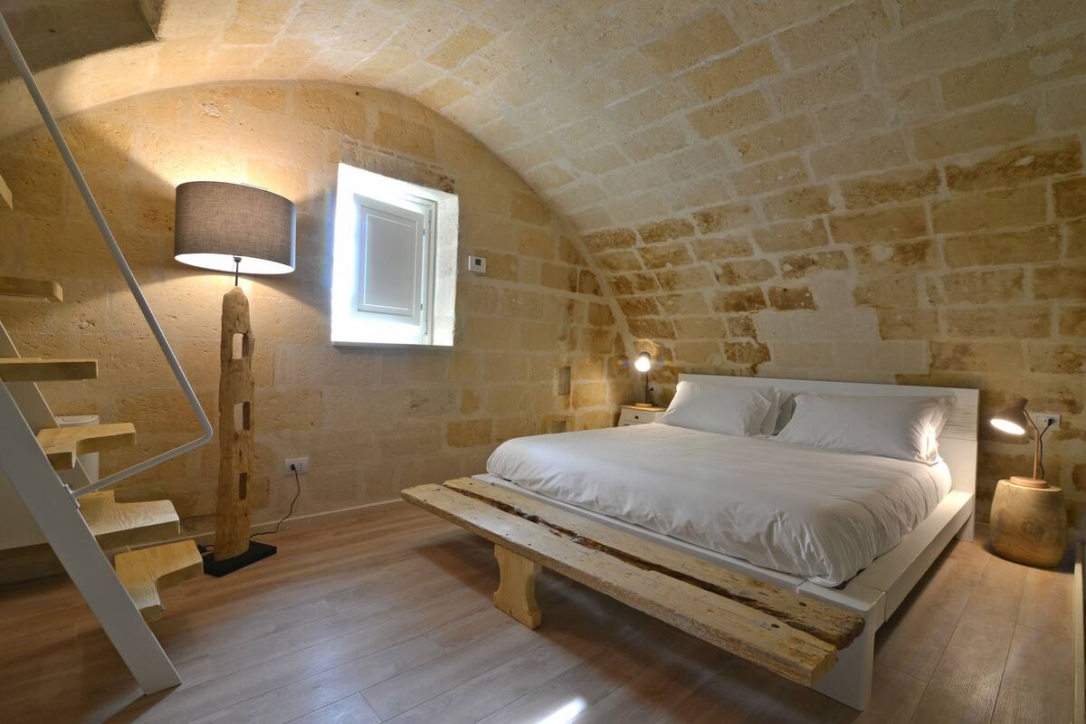A bedroom with a wooden bed, a wooden bench, a staircase, and a lamp.