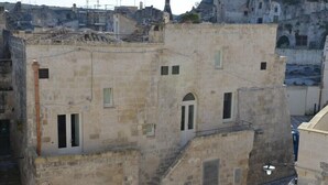 A stone building with multiple windows and a small staircase leading to an upper level. - Comera (Matera)