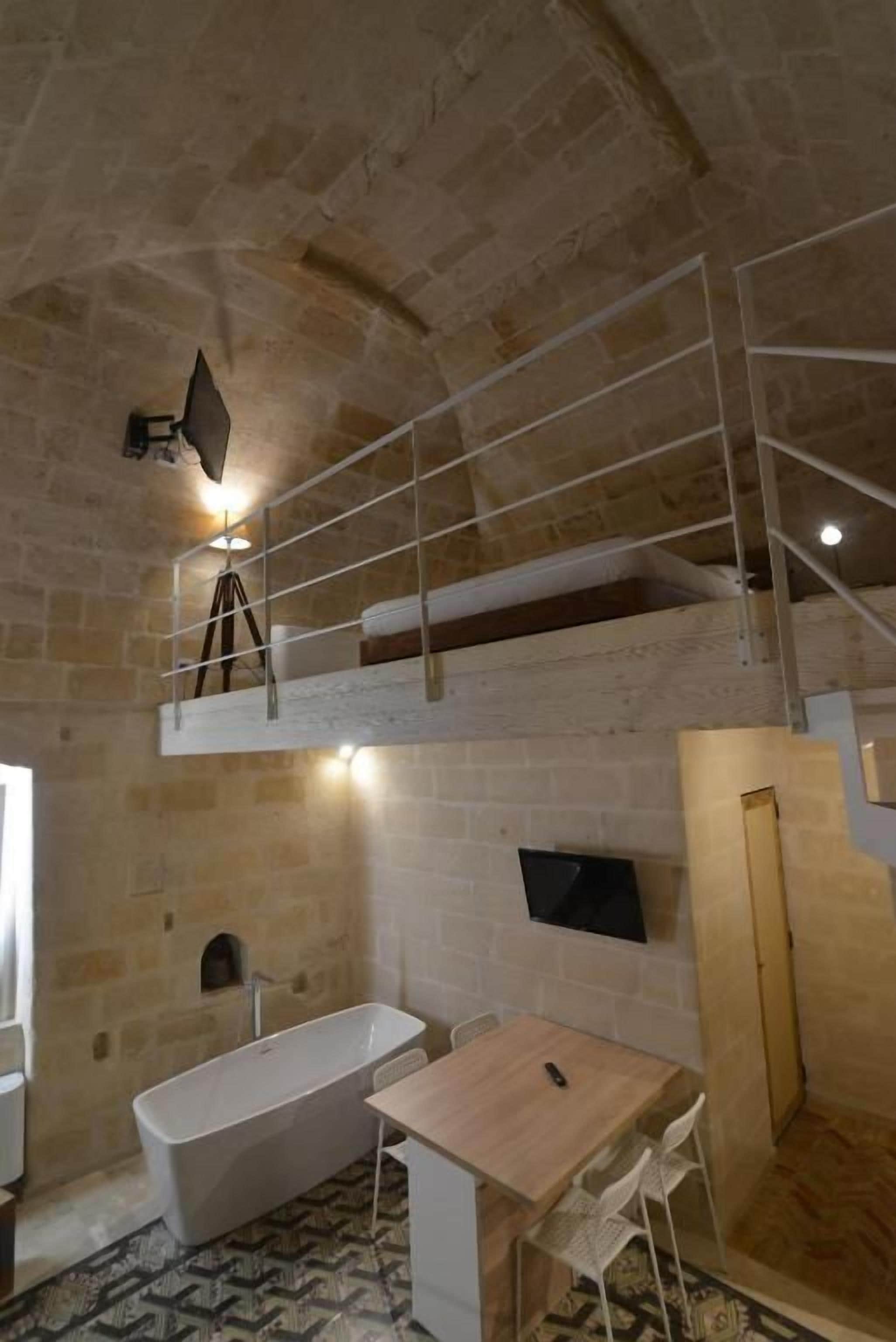 Une salle de bain aux murs de pierre, avec une baignoire, une table en bois et une chaise.