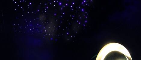 A person sitting on a bed with a laptop, a large circular light fixture, and a starry ceiling.