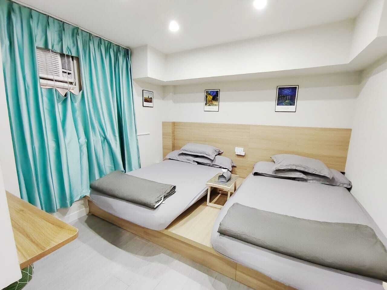 Une chambre d’hôtel avec deux lits, une tête de lit en bois, une petite table et une fenêtre avec des rideaux.