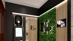 A modern lobby with a reception desk, a digital check-in kiosk, and a wall with a green leafy design. - The Nap Tsim Sha Tsui (Kowloon)