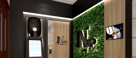 Een moderne lobby met een receptiebalie, een digitale incheckterminal en een wand met een weelderig, groen ontwerp.