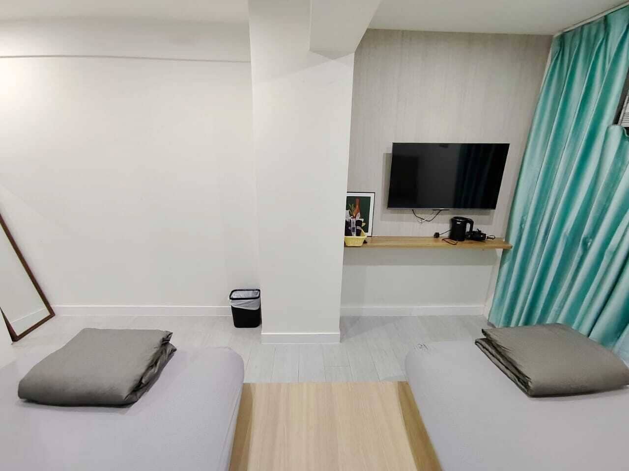 Une chambre d’hôtel avec deux lits simples, un téléviseur fixé au mur, une petite table et une poubelle.