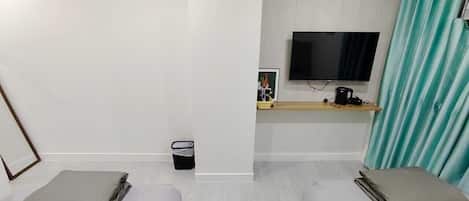 A hotel room with two single beds, a TV on the wall, a small table, and a trash bin.