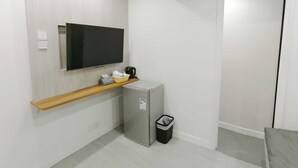 A small, modern room with a flat-screen TV mounted on the wall, a small refrigerator, a trash bin, and a wooden shelf with a coffee maker. - The Nap Tsim Sha Tsui (Kowloon)