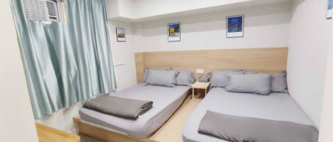 A modern hotel room with two single beds, a wooden headboard, a small bedside table, and a window with curtains.