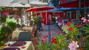 An outdoor cafe with tables and chairs, covered by umbrellas, and surrounded by plants and flowers. - Fritz Hotel (Weil am Rhein)