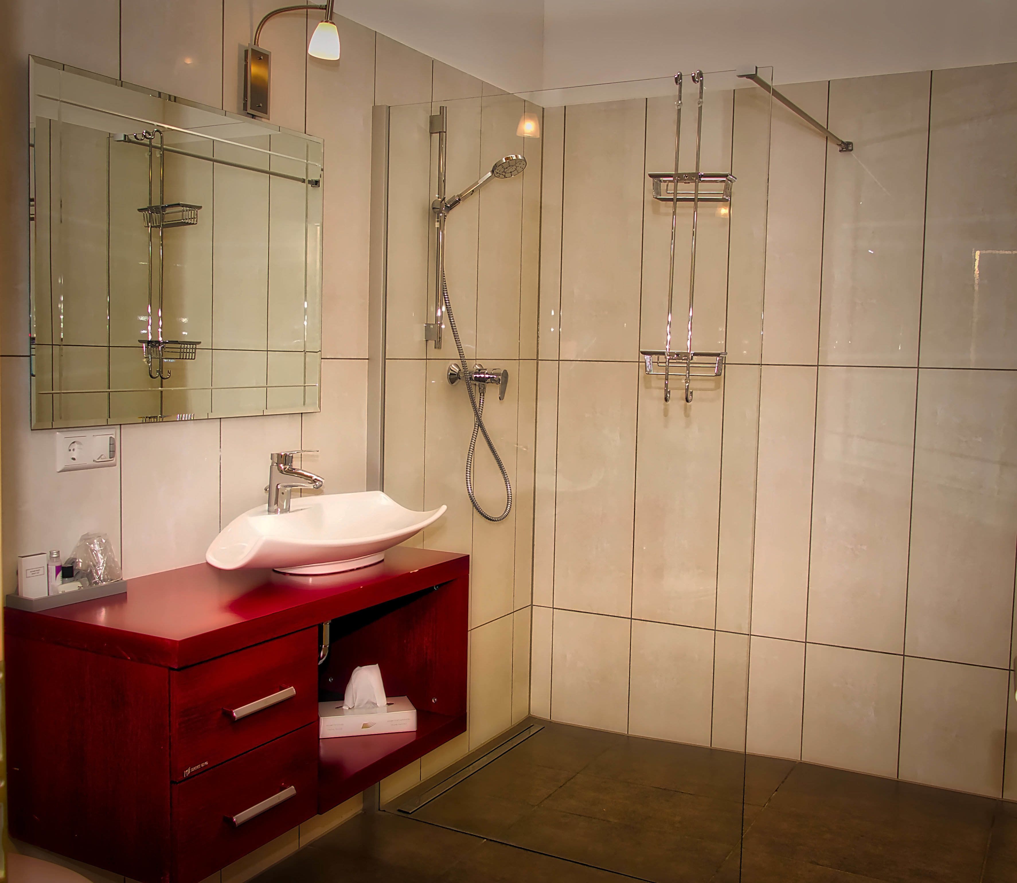 A modern bathroom with a large mirror, a red vanity, a white sink, and a glass shower enclosure.