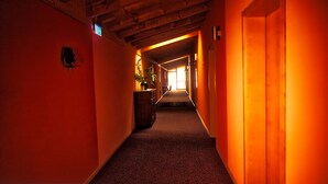A hallway with a wooden ceiling, a plant on a desk, and a door at the end. - Fritz Hotel (Weil am Rhein)