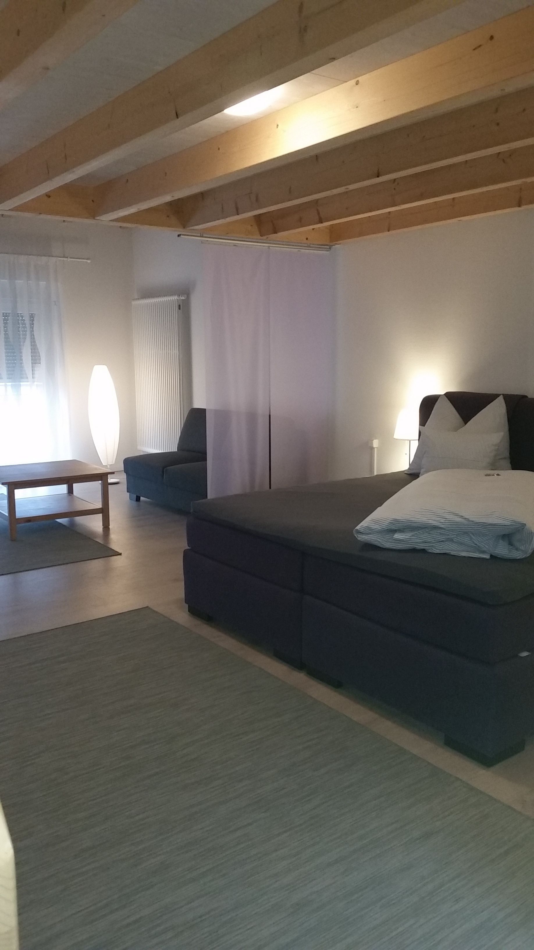 Un dormitorio moderno con una cama grande, un sofá, una mesa y una ventana con cortinas.