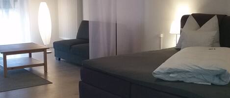 Un dormitorio moderno con una cama grande, un sofá, una mesa y una ventana con cortinas.