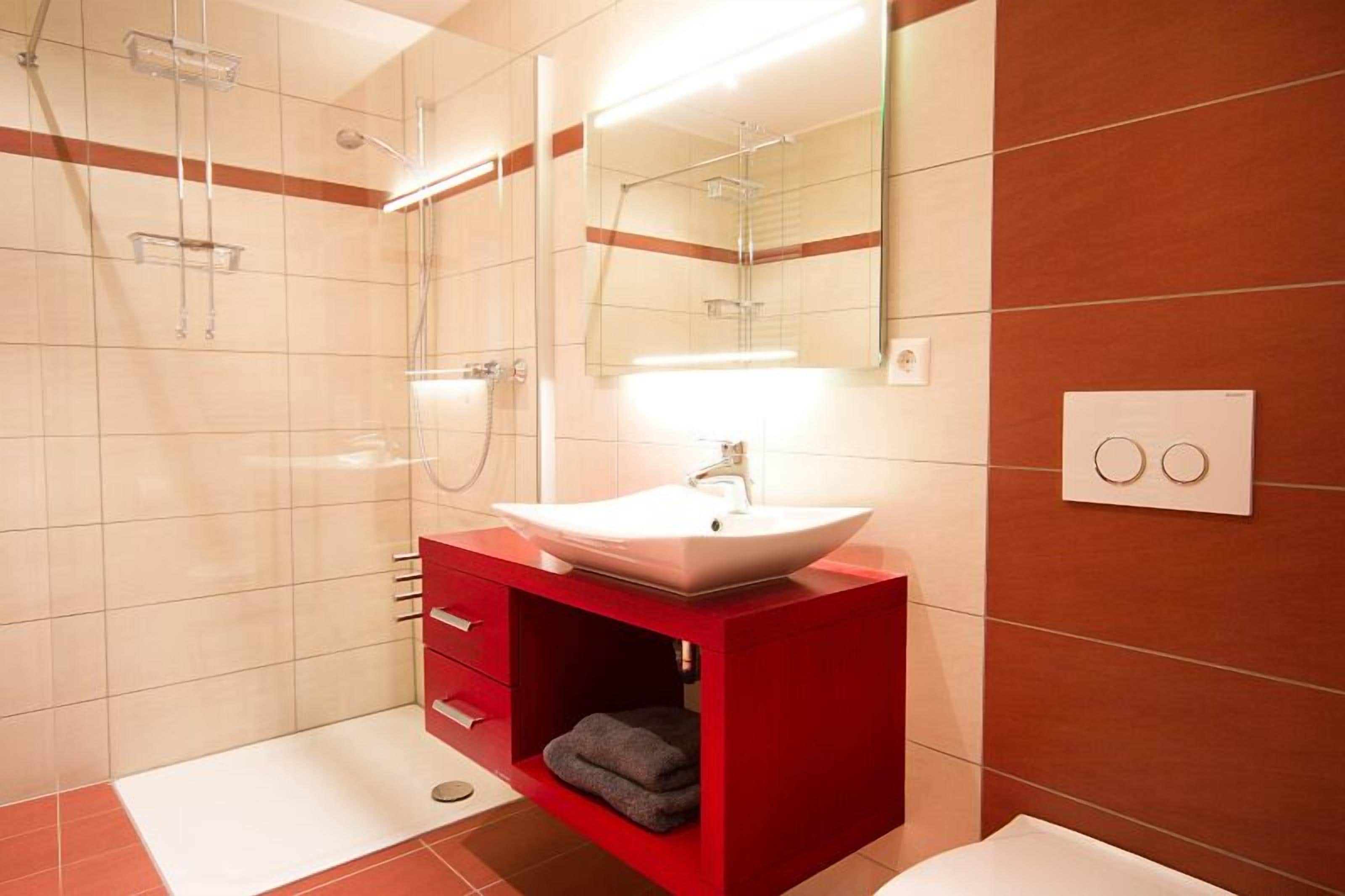 Un baño moderno con un tocador rojo, un lavabo blanco y un espejo grande.