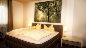 A hotel room with a large bed, two bedside lamps, a nightstand, and a painting of a forest. - Fritz Hotel (Weil am Rhein)