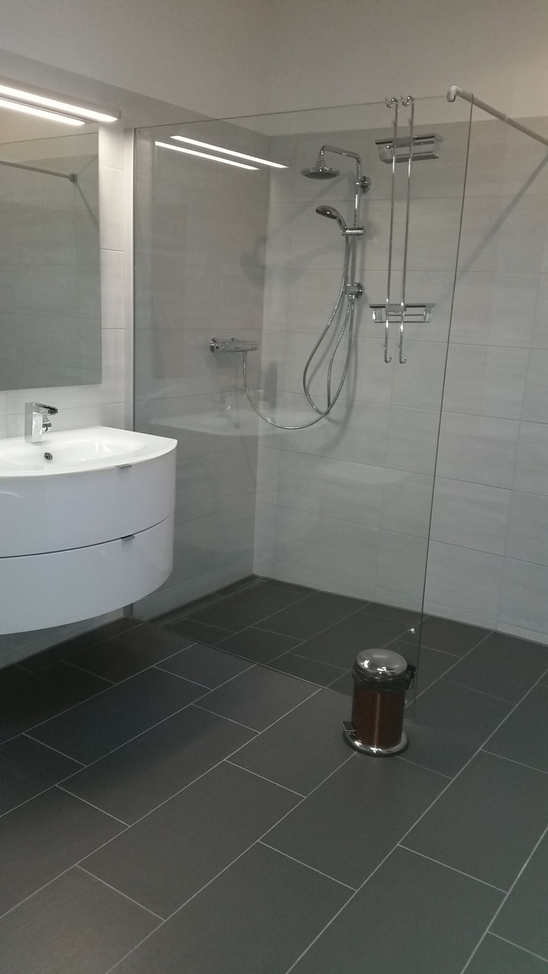 A modern bathroom with a white sink, a glass shower enclosure, and dark tiled flooring.