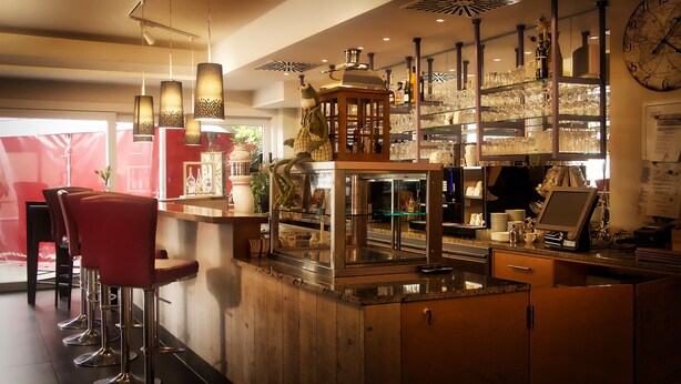 A bar area with stools, a wooden counter, and a display case. - Fritz Hotel (Weil am Rhein)