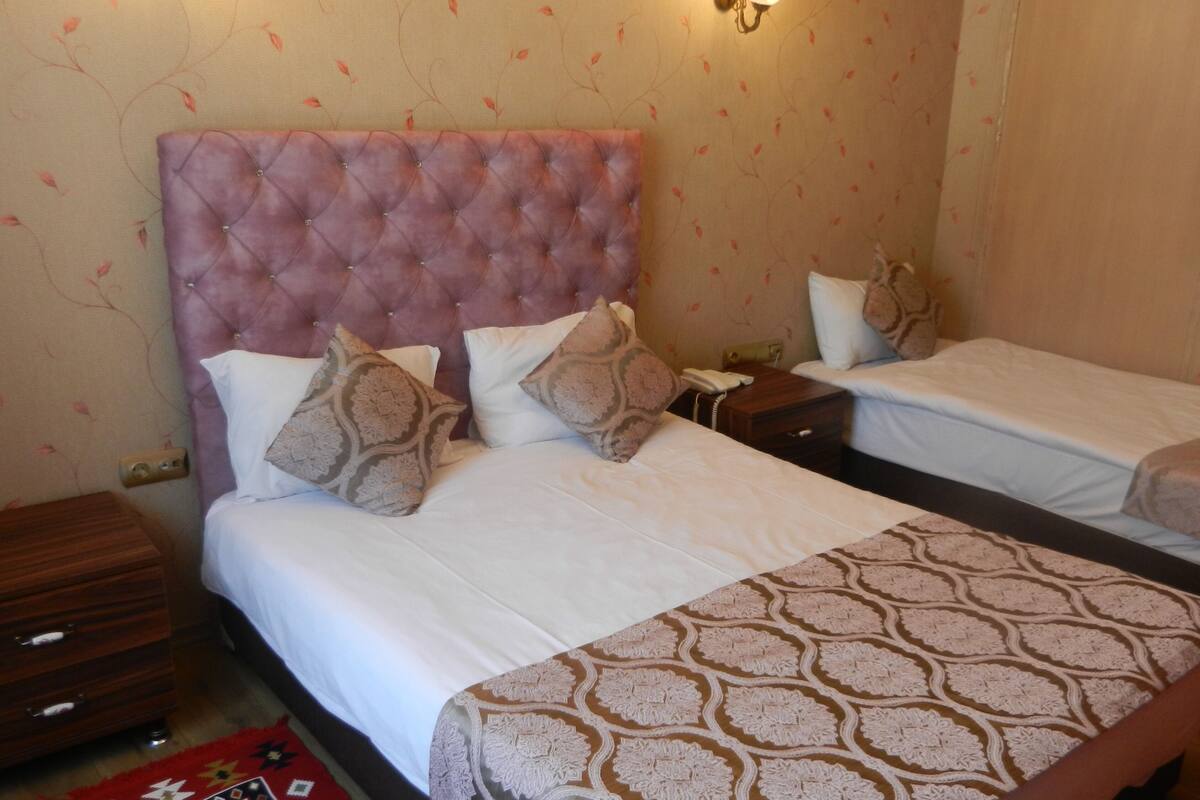 A hotel room with two beds, a wooden nightstand, a bedside table, and a patterned bedspread.
