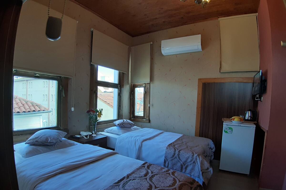 A room with two beds, a small kitchenette, and a window with a view of buildings.