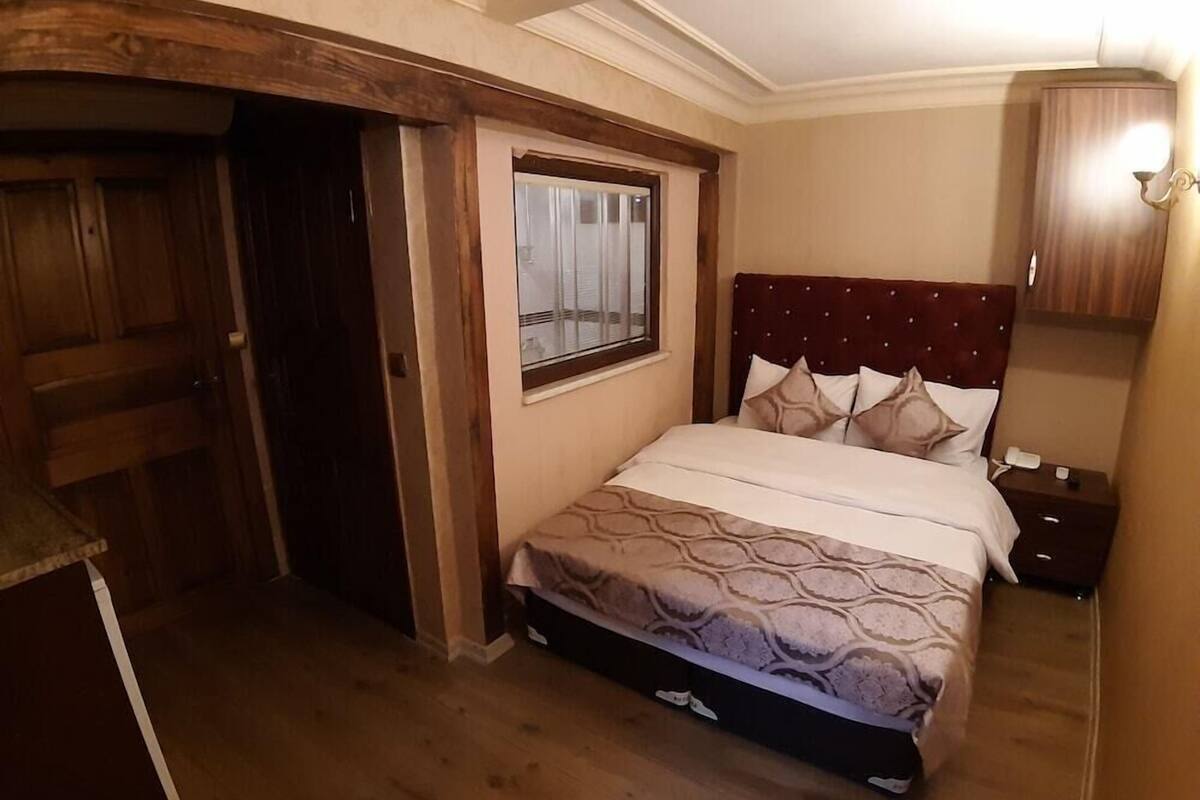 A bedroom with a bed, a window, a wooden door, and a nightstand.