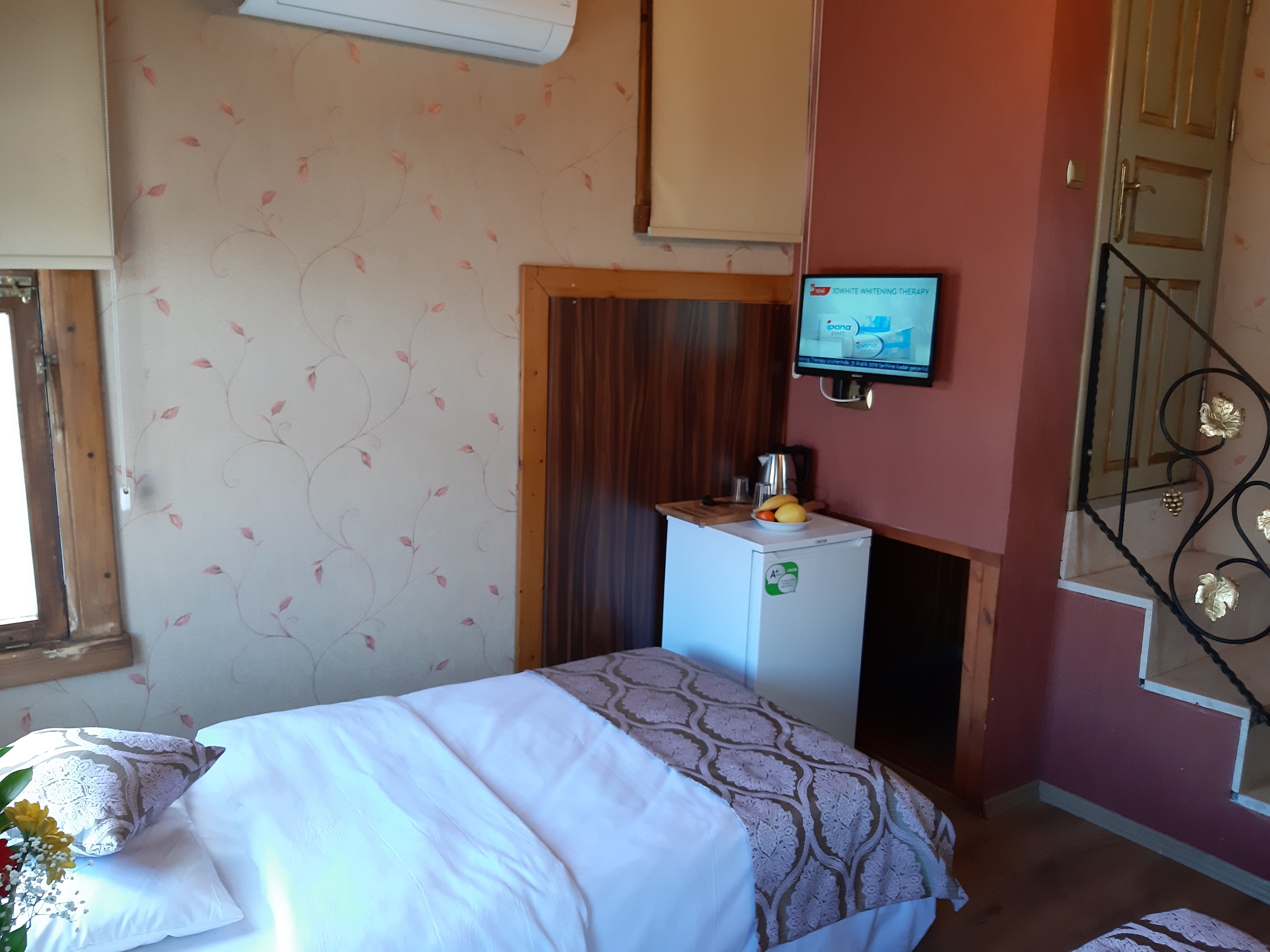 Une chambre avec un lit, un petit réfrigérateur, un téléviseur fixé au mur et une fenêtre avec des rideaux.