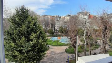 Vista da janela sobre um pátio com uma grande árvore perene, uma piscina e um conjunto de edifícios ao fundo.