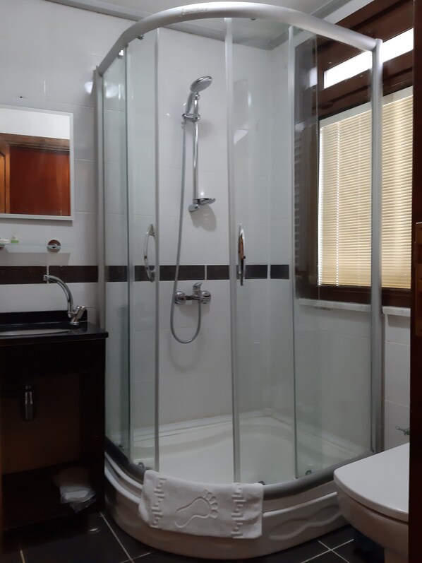 A glass-enclosed shower stall with a handheld showerhead and a wall-mounted faucet.