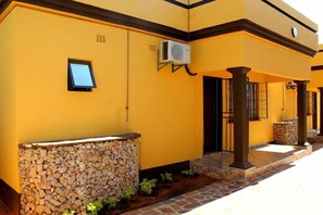 A building with yellow walls, a stone wall with wood logs, and a tiled walkway. - Best Inn Hotel (Palapye)