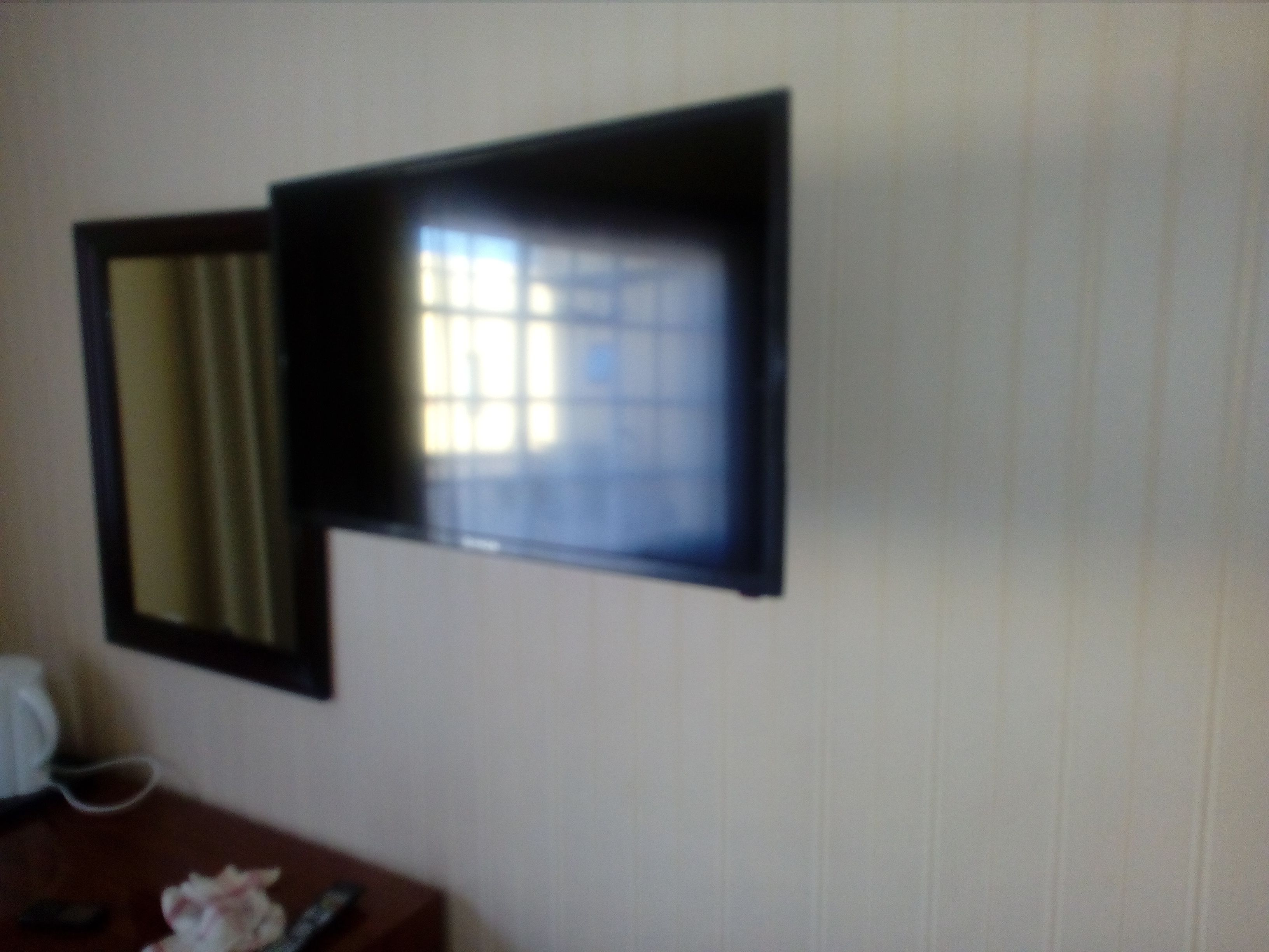 A room with a bed, a bedside table, a mirror, and a window with curtains.