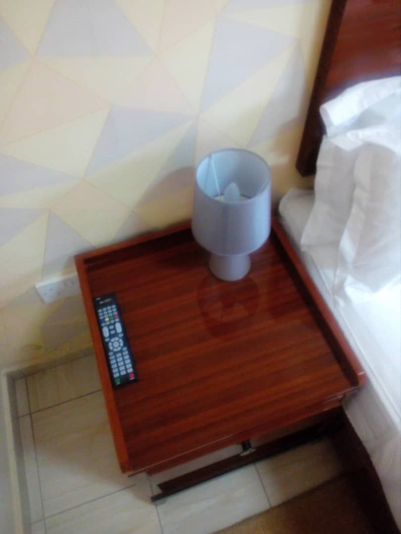 A wooden bedside table with a remote control and a lamp.