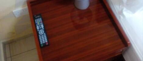 A wooden bedside table with a remote control and a lamp.