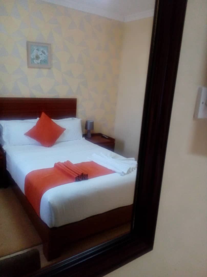 A neatly made bed with a red pillow and a white blanket, a nightstand with a lamp, and a framed picture on the wall.