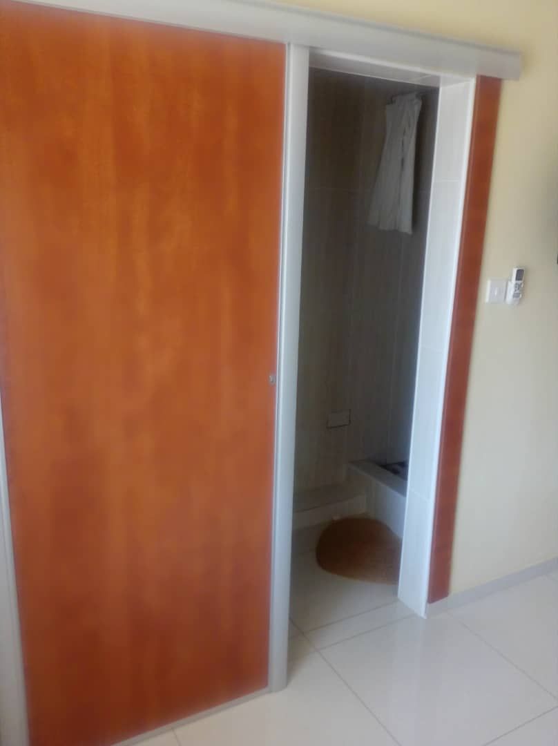 Ein Zimmer mit Holztür, gefliestem Boden und einer sichtbaren Duschkabine.