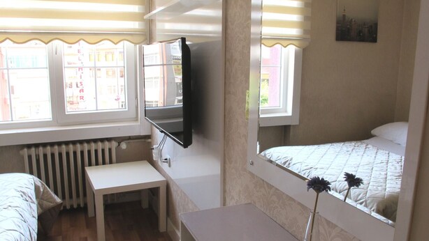 A room with a bed, a desk, a chair, a radiator, a TV, and a window with blinds. - Idrisoglu Hotel (Kastamonu)