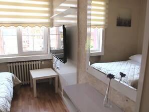 Una habitación con cama, escritorio, silla, radiador, televisor y ventana con persianas.