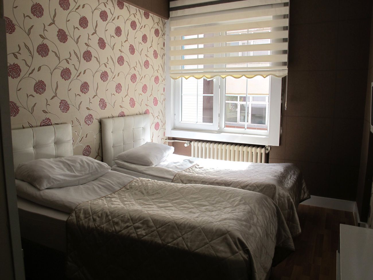 A bedroom with two beds, a radiator, and a window with blinds.