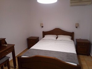 Een slaapkamer met een houten bed, twee nachtkastjes, een bureau en een lamp.
