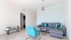 Una sala de estar moderna con un sofá gris, un sillón azul, una mesita redonda y una lámpara colgante.