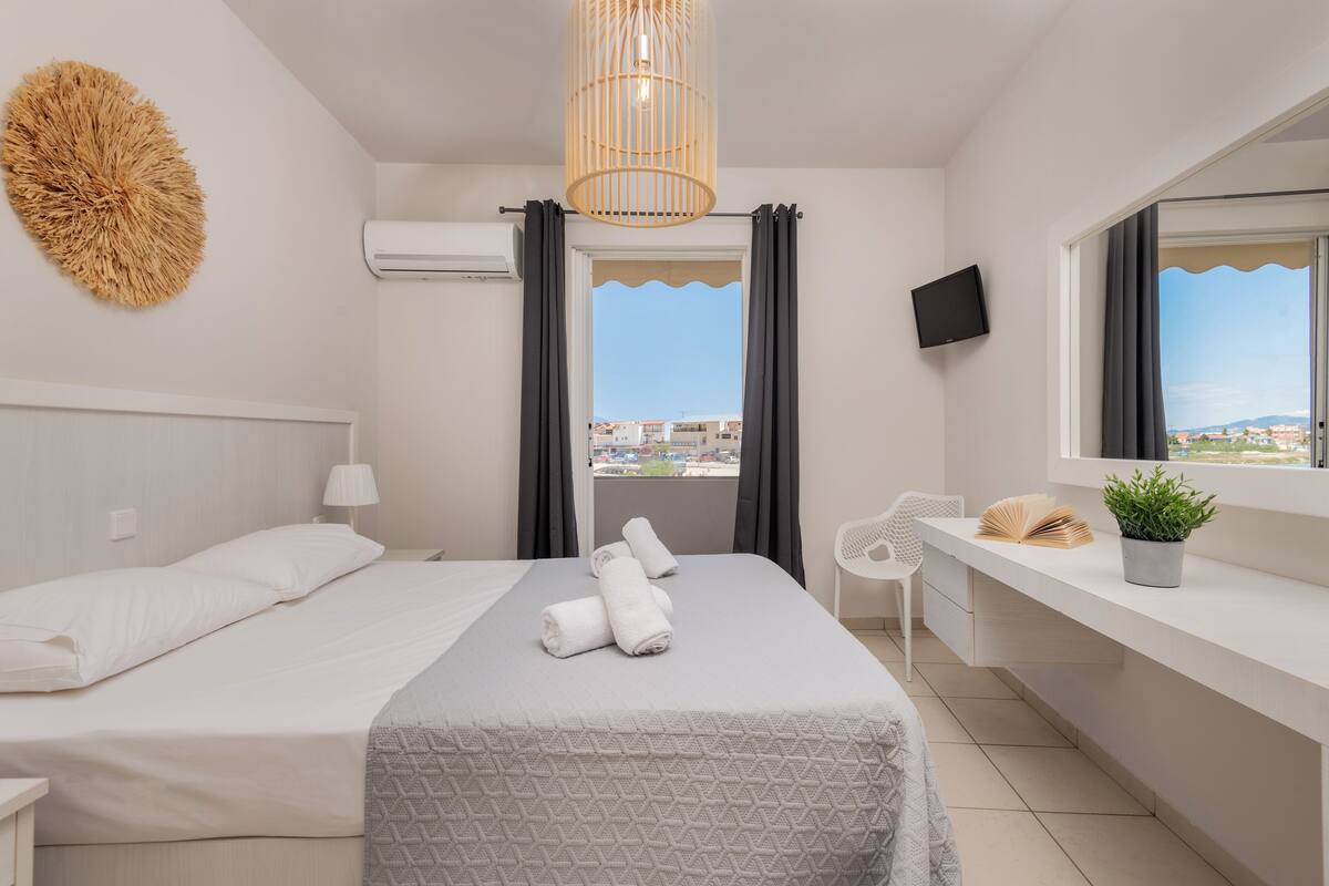 A hotel room with a bed, a desk, a TV, a window with curtains, and a view of the city.
