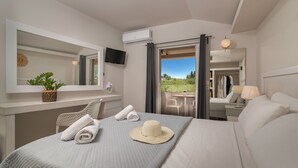 Une chambre d’hôtel comprenant un lit, un bureau, une chaise, une télévision, un balcon avec une table et des chaises, et une vue sur la verdure.