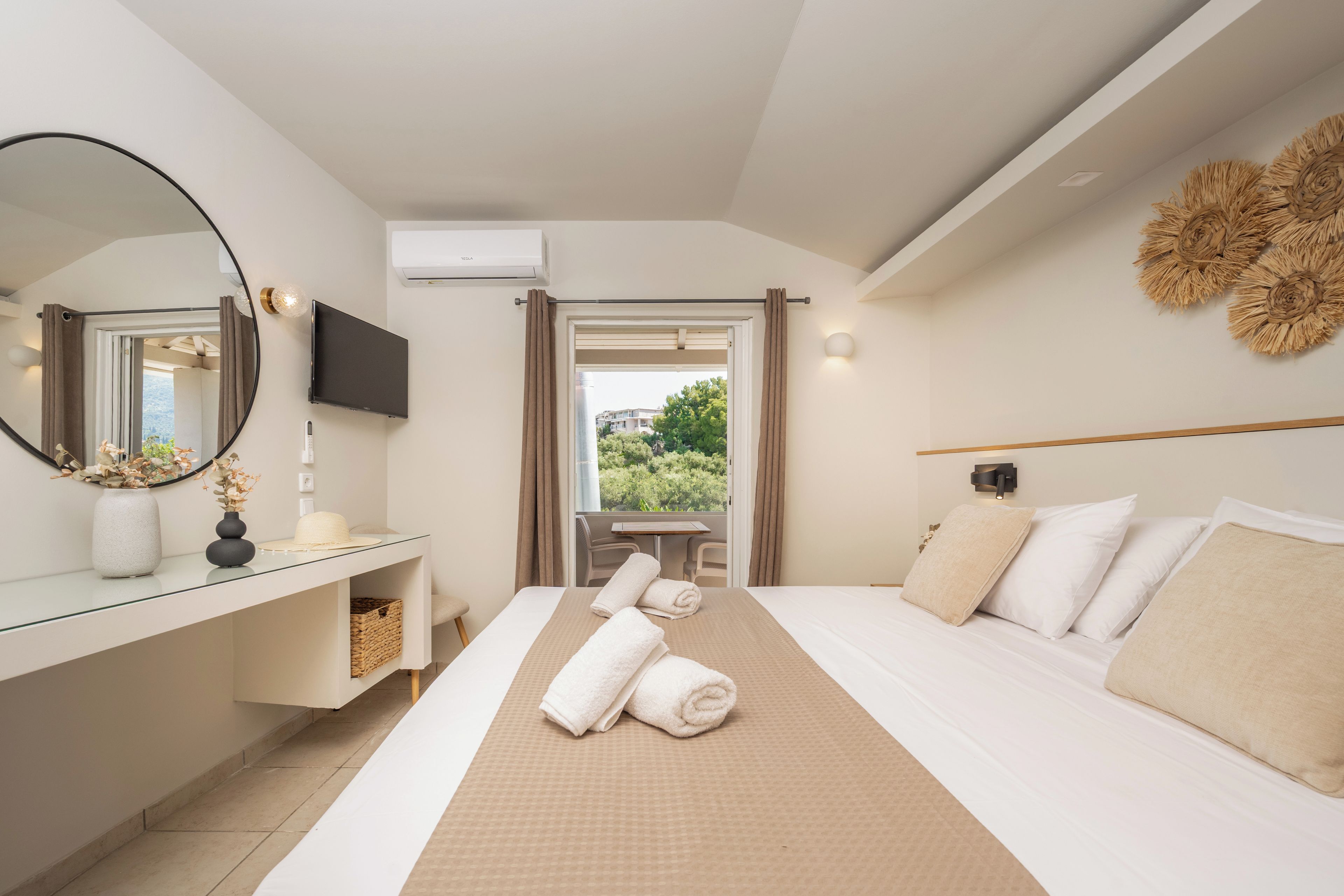 A hotel room with a bed, bedside table, mirror, TV, and a view of greenery outside.